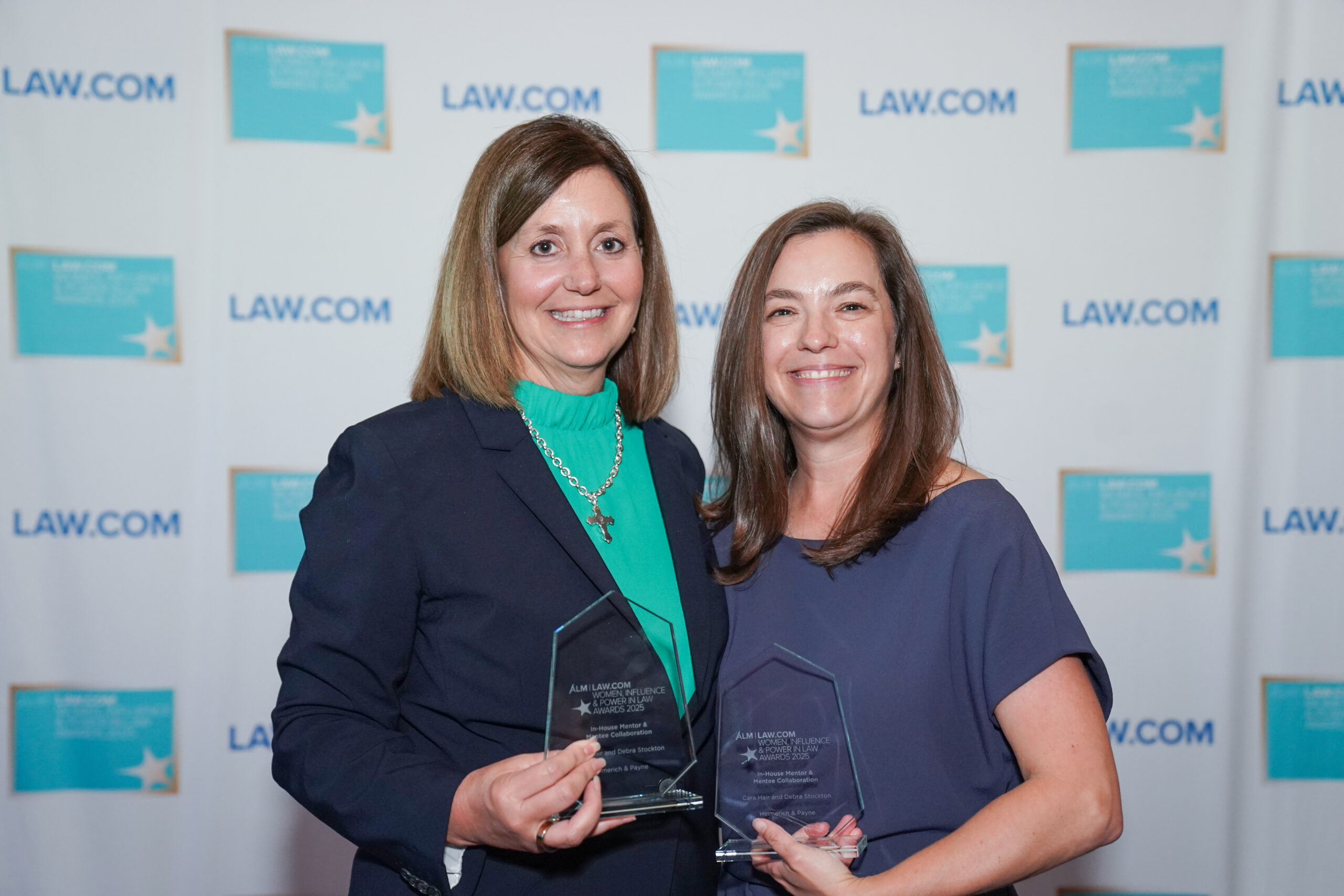 Debra Stockton and Cara Hair holding awards in front of a Law.com banner